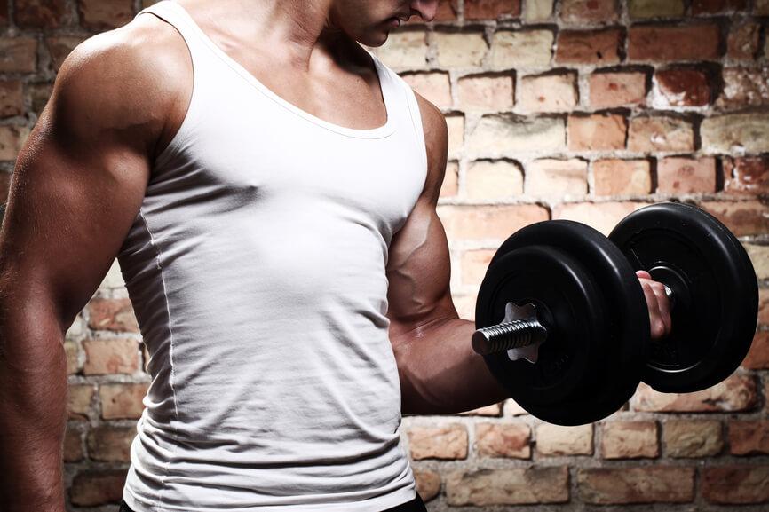Muscular guy doing exercises with dumbbell against a brick wall